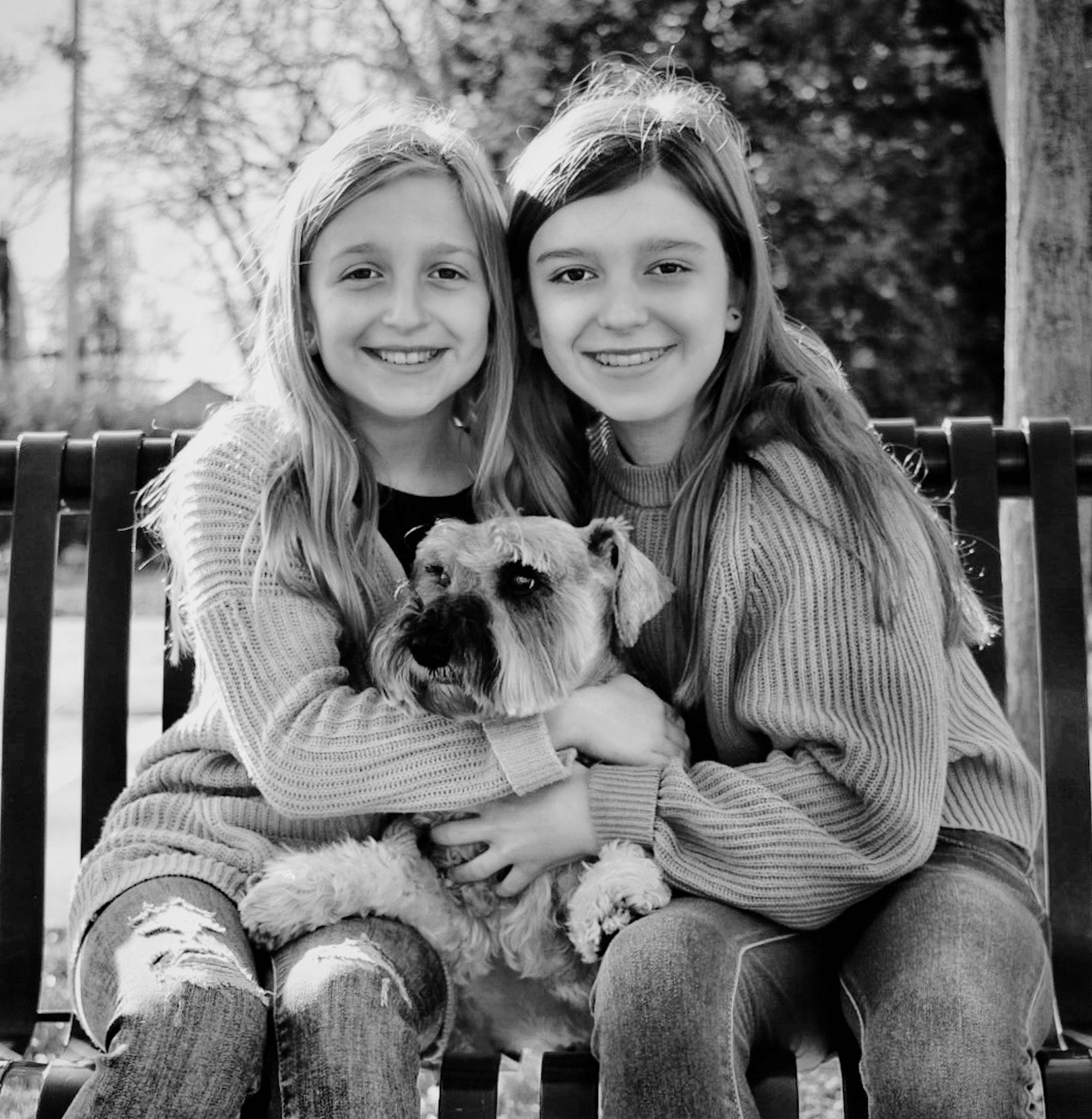 Two young girls, sisters, holding a dog